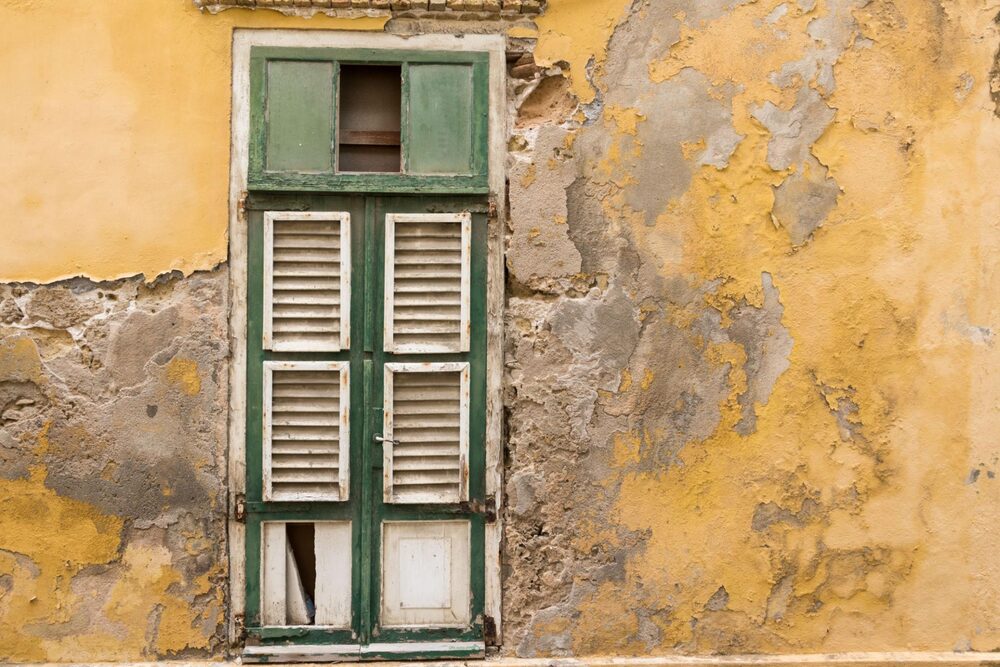 A weathered yellow Curaçao facade with a green shuttered window — the island's heritage and the long-term future that sustainable business decisions help protect